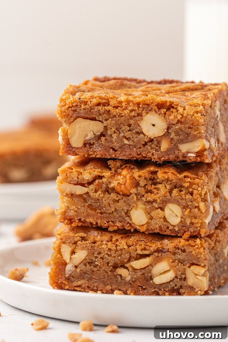 Stack of three rich, chewy brown butter blondies on a white plate, showcasing their golden edges and speckled interior.