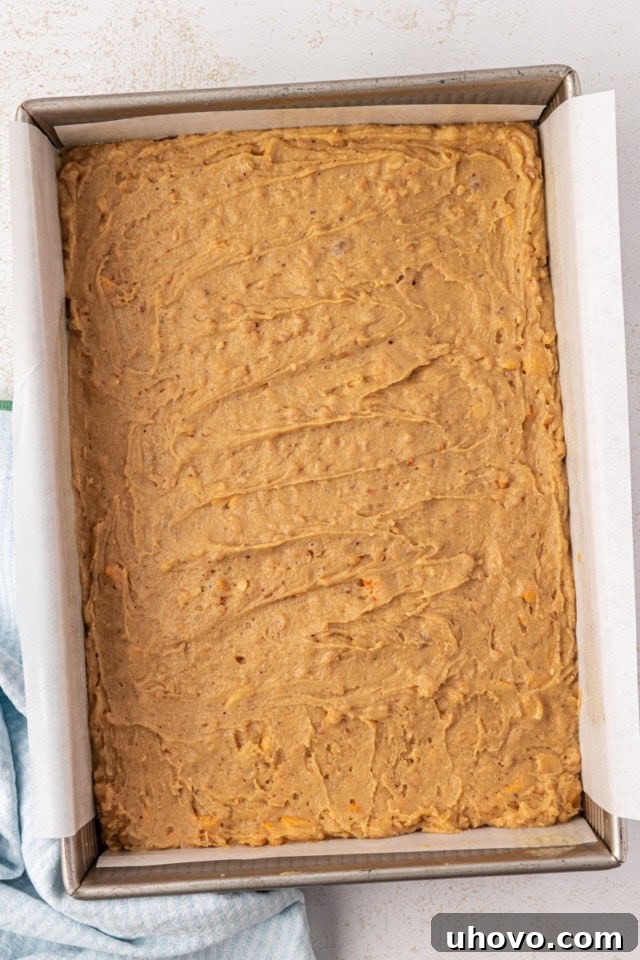 Overhead view of brown butter blondie batter smoothly spread into a parchment-lined 9x13 baking pan, ready to be placed in the oven.