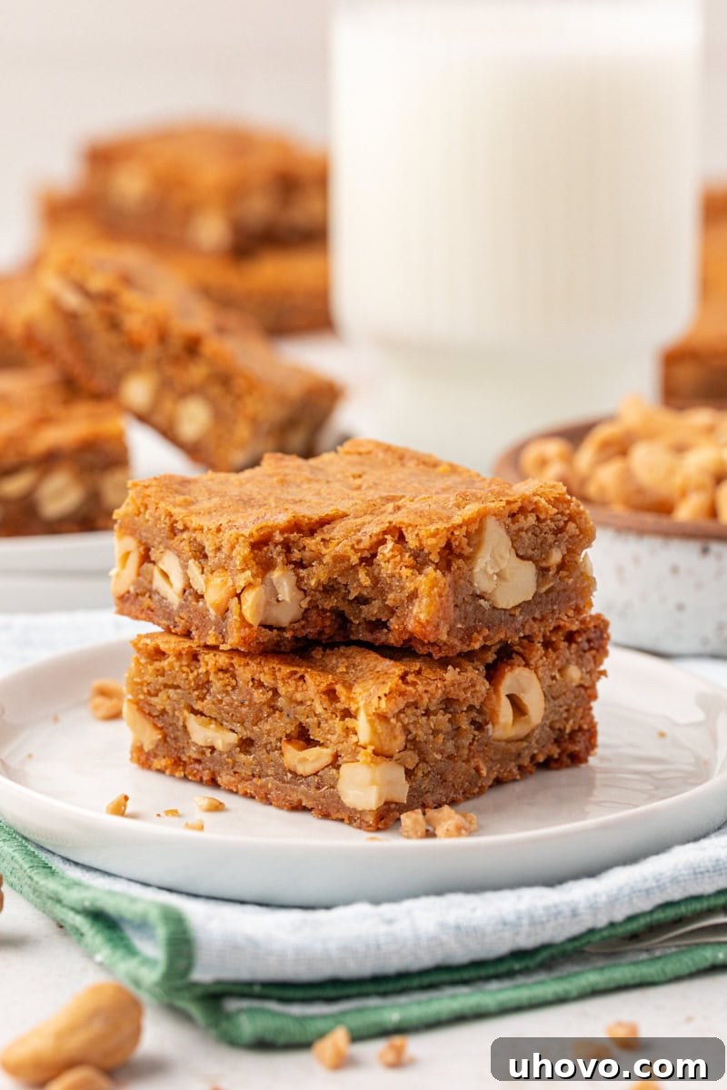 A stack of two brown butter blondies on a white plate, with a bite playfully taken from the top bar, revealing its soft, chewy interior.
