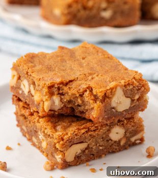 Two brown butter blondies stacked on a white plate with a bite missing from the top bar.