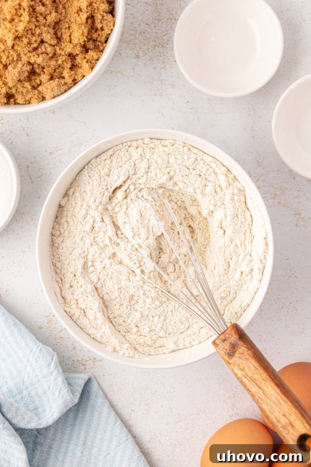Overhead view of all-purpose flour, baking powder, and salt precisely measured and mixed in a white bowl.