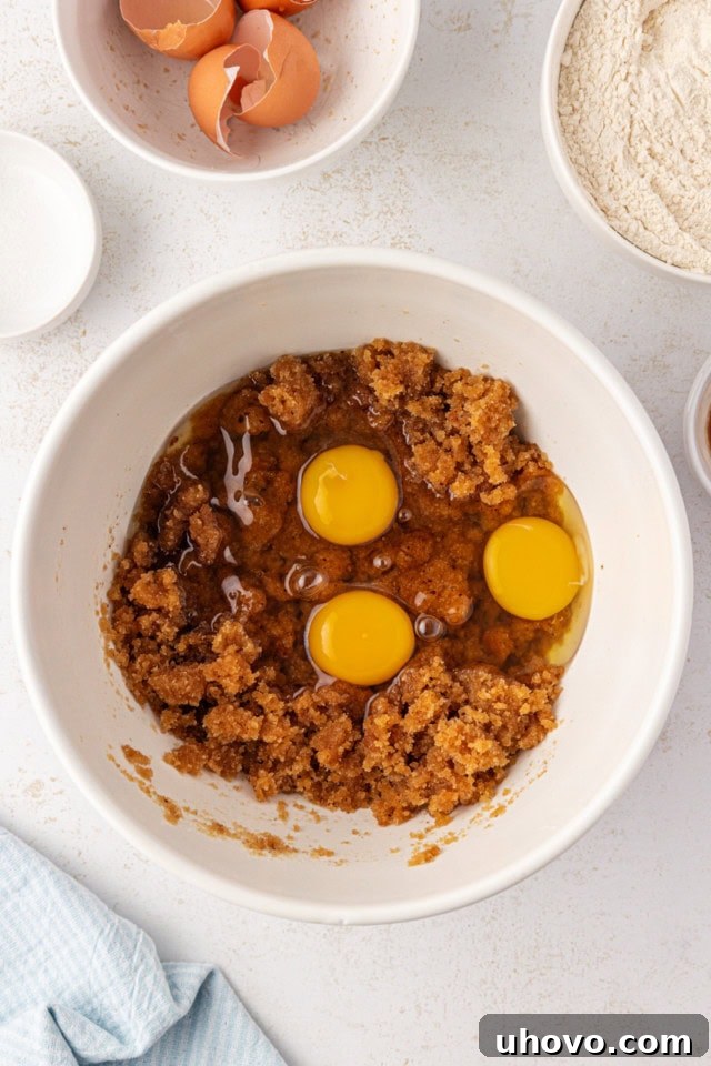 Overhead view of eggs being cracked and added to the blondie batter mixture in a bowl.
