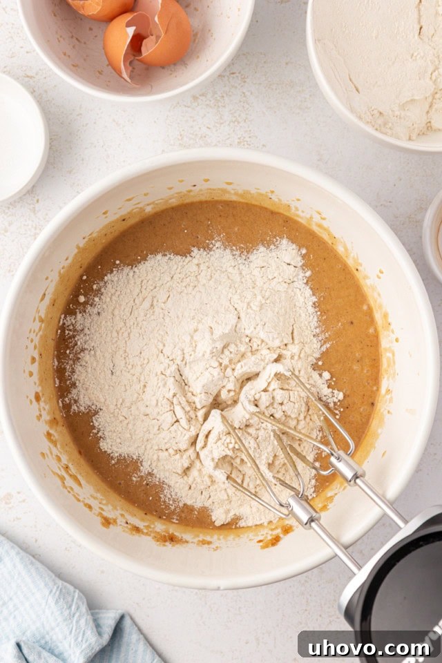 Overhead view of dry ingredients being carefully added in portions to the wet ingredients for brown butter blondies in a large mixing bowl.
