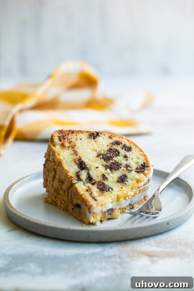 A perfectly sliced piece of moist chocolate chip almond cake on a delicate plate, ready to be enjoyed with a fork beside it.