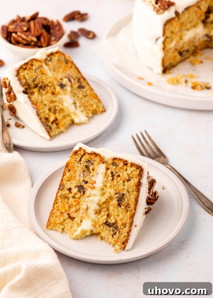 two slices of carrot cake served on light beige plates with the remaining cake and a bowl of pecans in the background