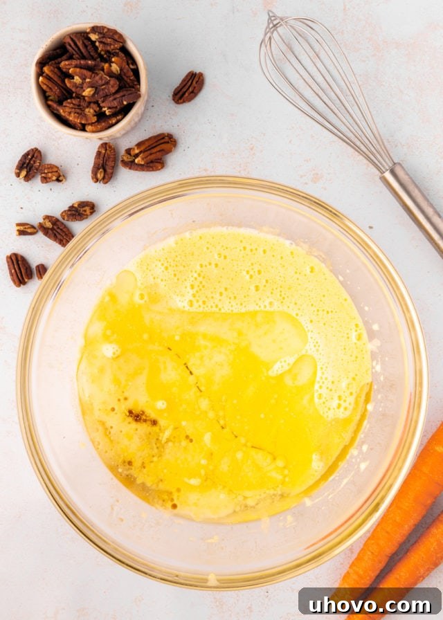 overhead view of oil, buttermilk, and vanilla extract added to beaten sugar and eggs in a glass mixing bowl