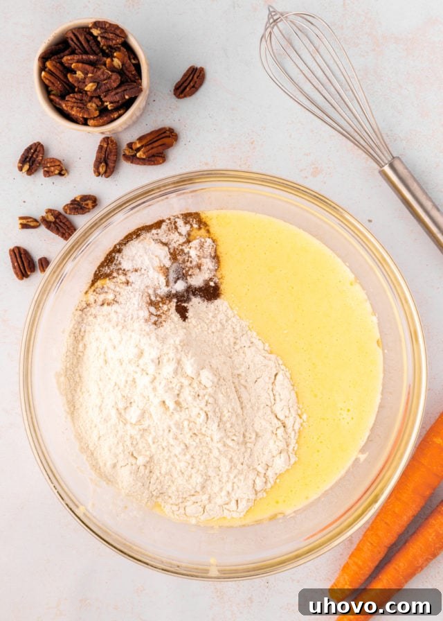 overhead view of flour, baking powder, cinnamon, nutmeg, cloves, and salt added to cake batter in a glass mixing bowl