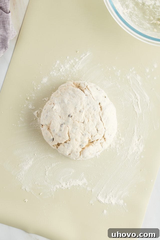 The Irish soda bread dough is neatly shaped into a rustic, round loaf on a floured surface, demonstrating perfect form before baking.