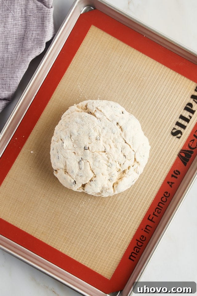 A perfectly shaped round loaf of Irish soda bread dough is placed onto a baking sheet lined with a silicone mat, ready for scoring and baking.