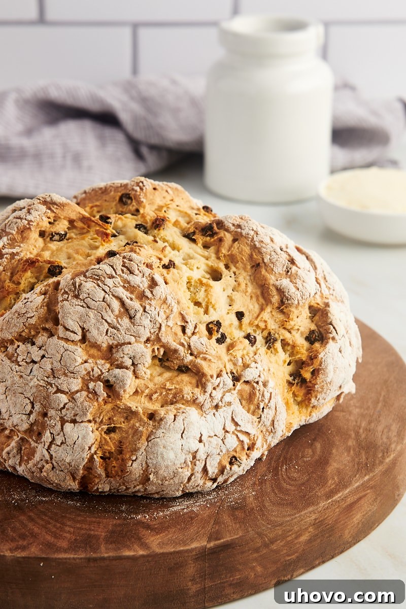 A pristine, unsliced round loaf of Irish soda bread rests elegantly on a light wooden board, showcasing its perfectly golden, crusty top.
