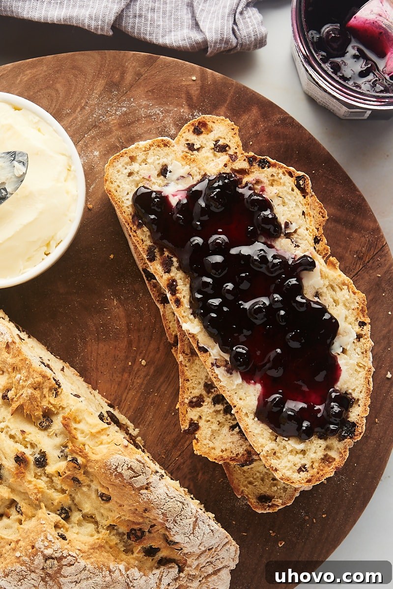 A delectable slice of Irish soda bread generously spread with butter and blueberry preserves, accompanied by more bread, butter, and preserves.