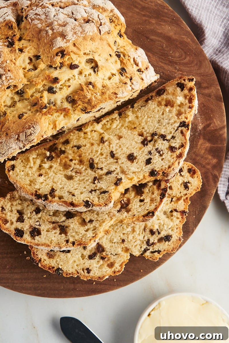 A partially sliced, round Irish soda bread on a wooden board, with a small bowl of soft butter for serving nestled beside it.