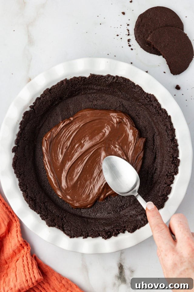 Spoon spreading a thin chocolate layer over the pie crust