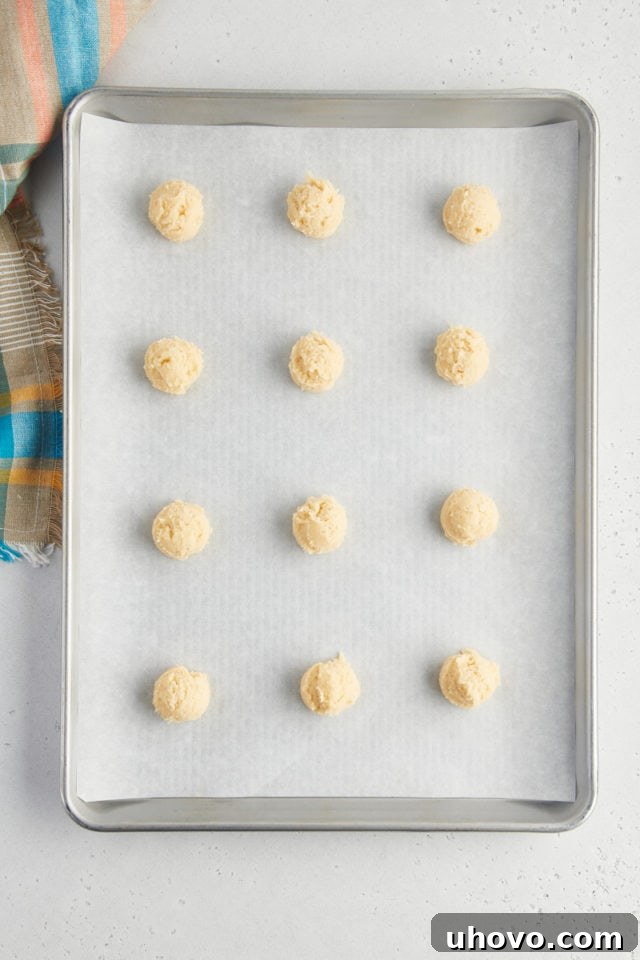 overhead view of sour cream cookie dough scooped onto a baking sheet lined with parchment paper
