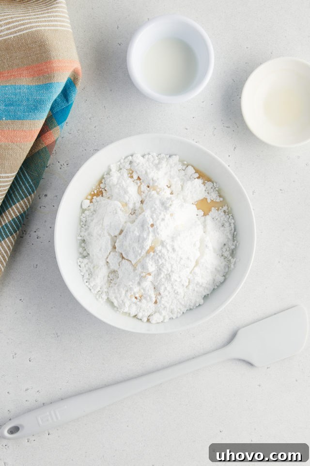 overhead view of confectioners' sugar, vanilla extract, and milk in a white mixing bowl