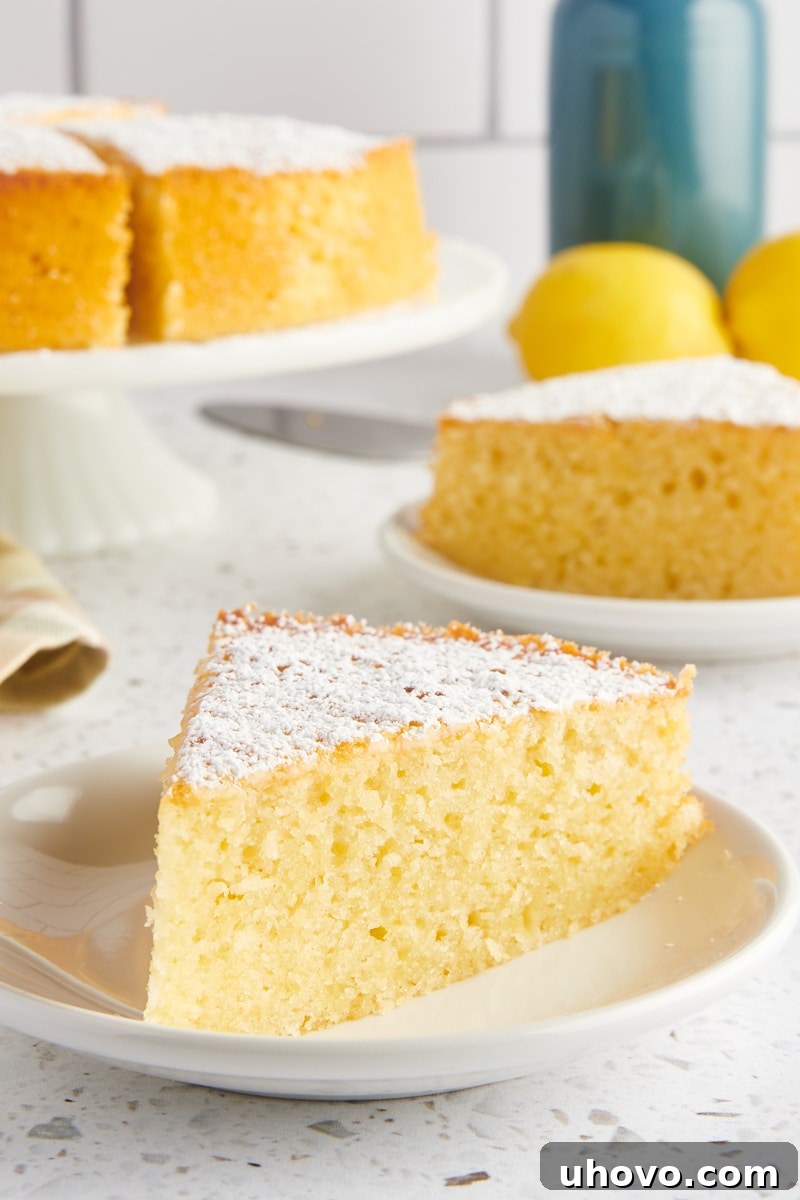 a slice of olive oil cake on a white plate with more cake on a cake stand and on a plate in the background