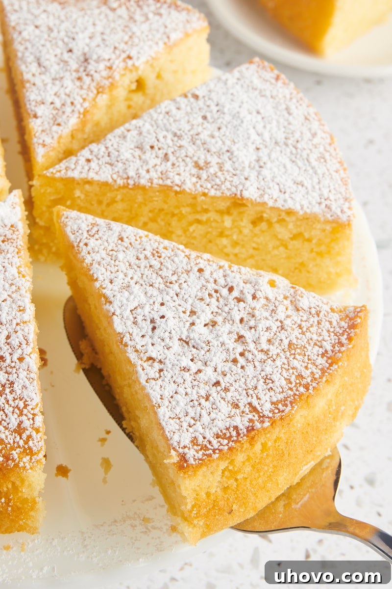 a slice of olive oil cake on a cake server being lifted away from the remaining cake on a cake stand
