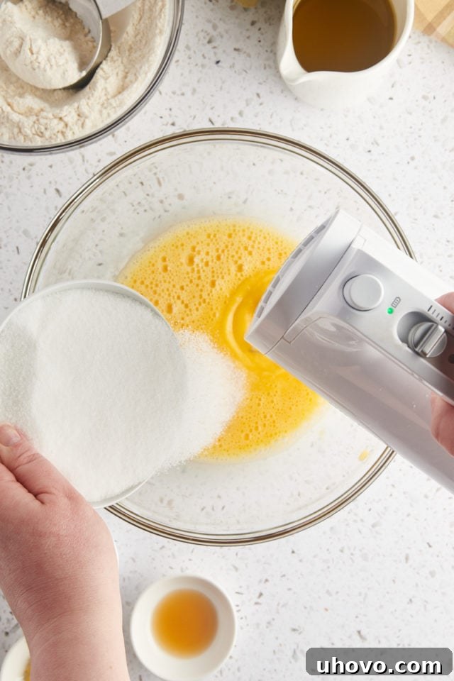 overhead view of sugar gradually being added to beaten eggs in a glass mixing bowl