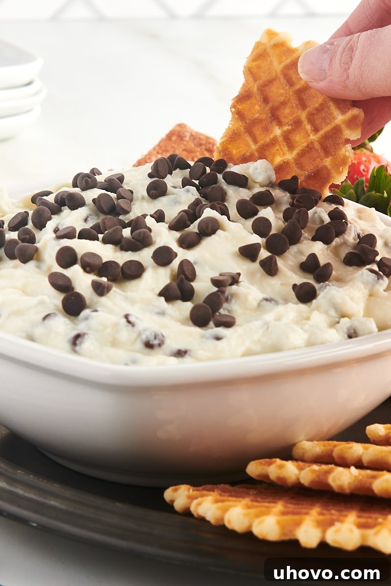 a waffle cookie being dipped into a bowl of cannoli dip