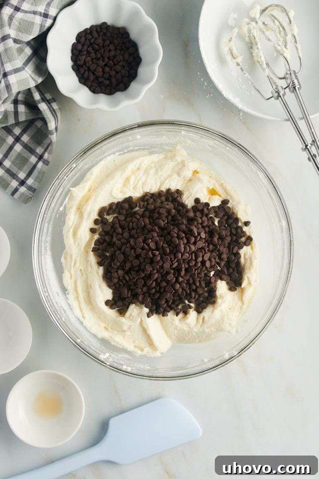 overhead view of mini chocolate chips added to cannoli dip in a glass mixing bowl