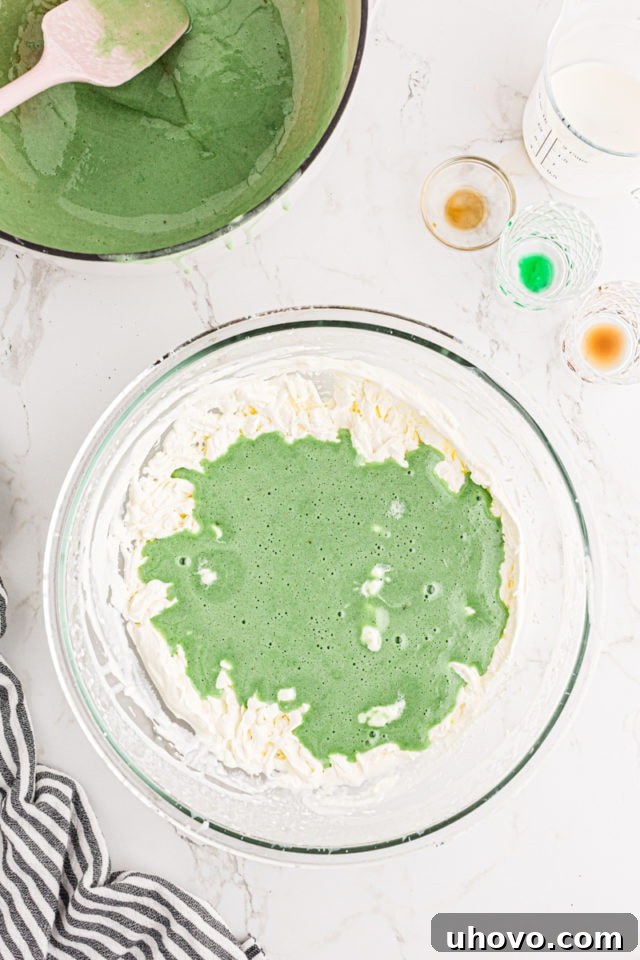 The vibrant green marshmallow mixture being carefully folded into the light and airy whipped cream in a glass mixing bowl.