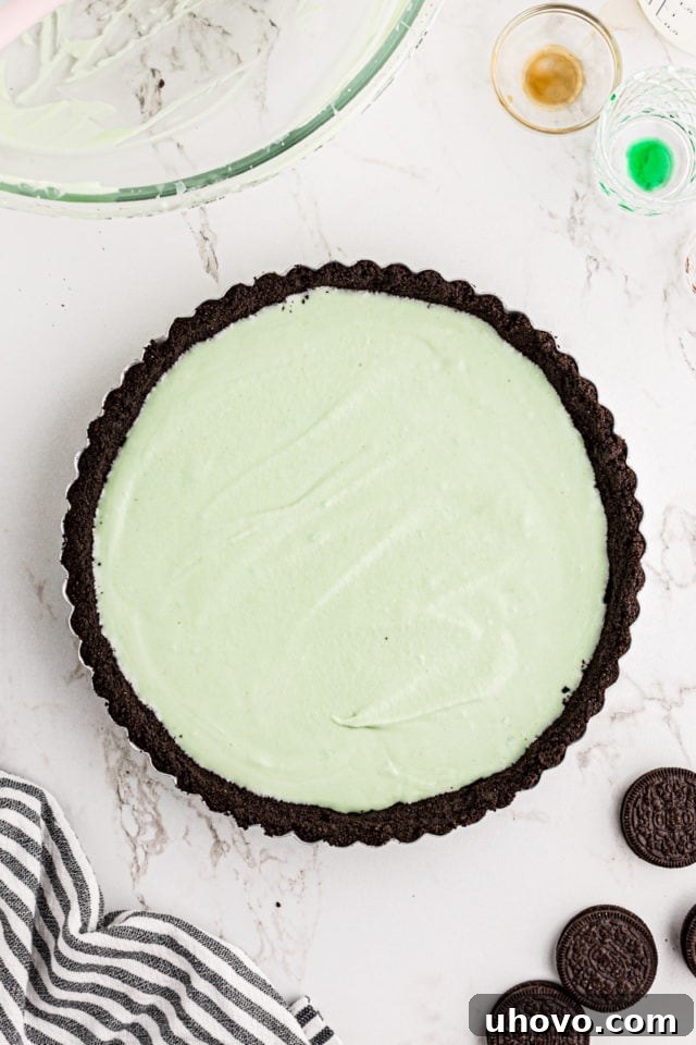 An overhead shot of the Grasshopper Pie filling being smoothly spread into the baked chocolate cookie crust within a tart pan, creating an even layer.