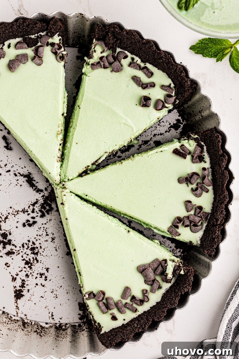 Four perfectly sliced portions of Grasshopper Pie, showcasing the vibrant green filling and dark chocolate crust, sitting invitingly in a metal tart pan.