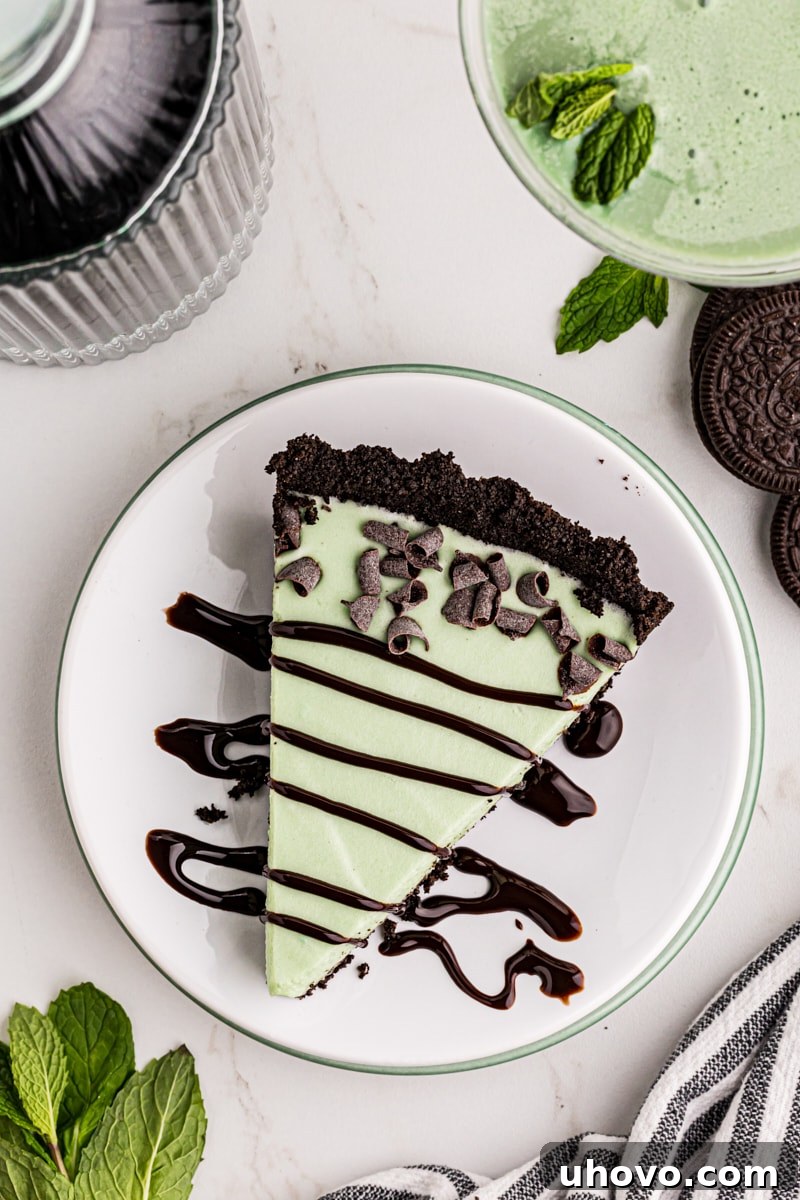 A beautifully composed overhead shot of a single slice of Grasshopper Pie, elegantly garnished with delicate chocolate curls and a generous drizzle of rich chocolate syrup.