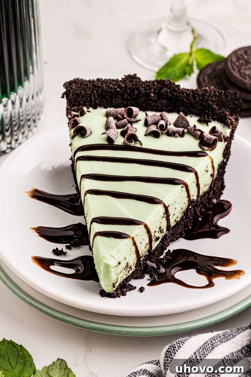 A close-up shot of a single slice of Grasshopper Pie on a white plate, richly topped with delicate chocolate curls and a luscious drizzle of chocolate syrup.