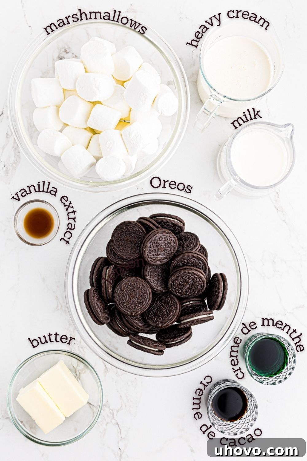 An overhead shot showcasing all the essential ingredients laid out for making a delicious Grasshopper Pie, including chocolate cookies, butter, milk, marshmallows, liqueurs, and heavy cream.