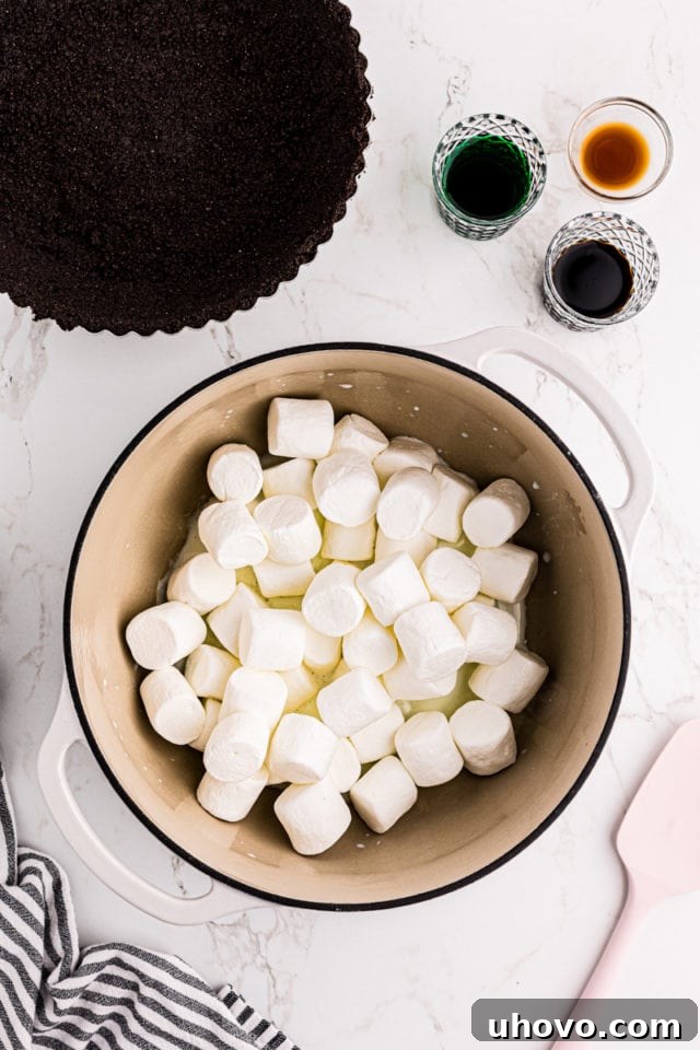 An overhead view showing butter and marshmallows melting together in a large, heavy-bottomed saucepan, creating a smooth, gooey mixture.