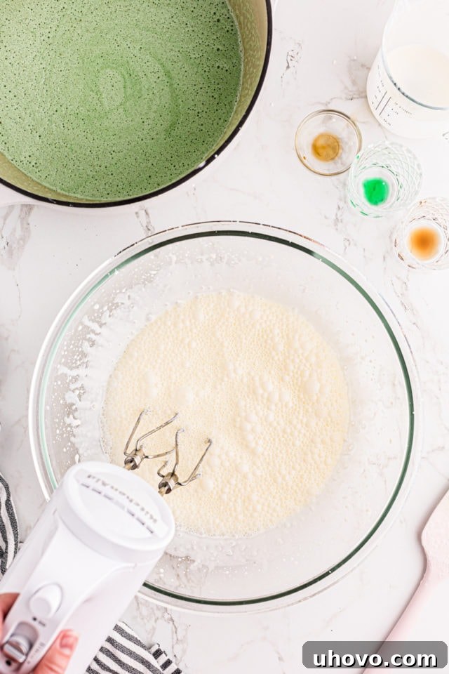 An overhead view of heavy cream being whipped in a clear glass mixing bowl, steadily transforming into stiff, fluffy peaks.