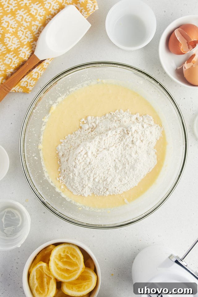 Overhead view of flour added to bowl of wet ingredients for lemon loaf