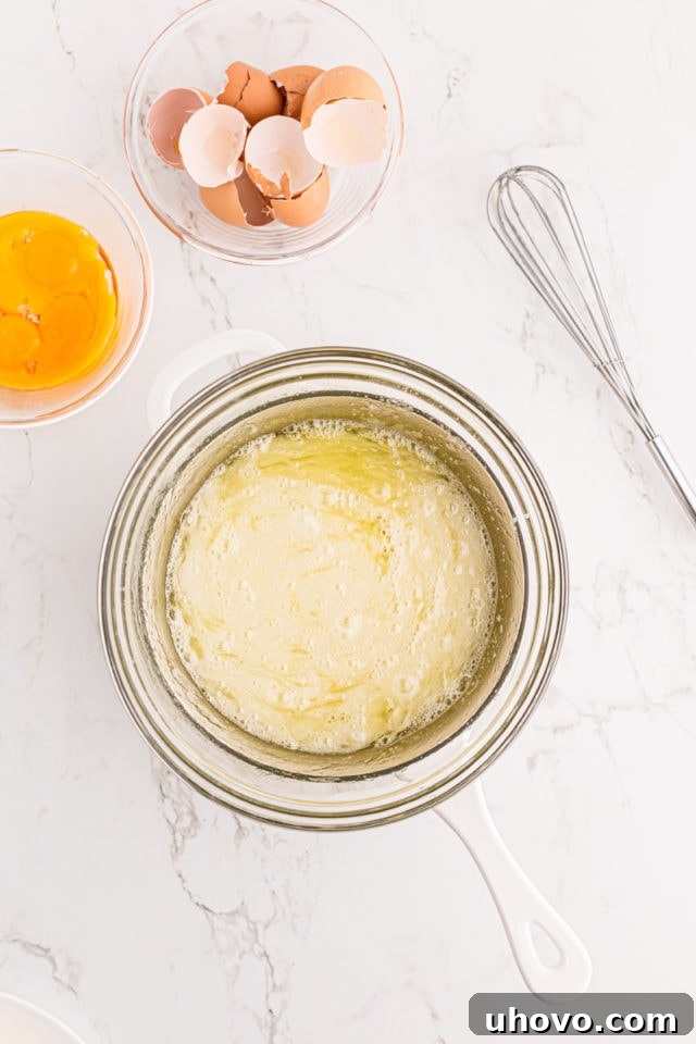 Overhead view of egg whites and granulated sugar in a heatproof glass bowl placed over a pot of simmering water (double boiler setup).
