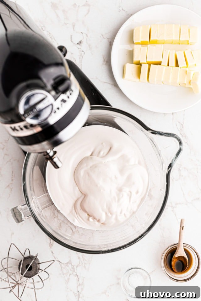 Overhead view of whipped egg whites and sugar in the bowl of a stand mixer, forming stiff, glossy peaks.