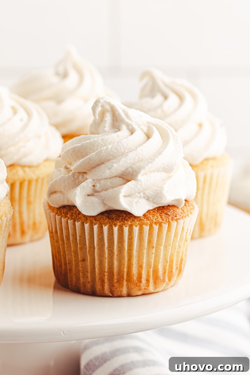 A cluster of beautifully frosted vanilla cupcakes elegantly arranged on a classic white cake stand, inviting viewers to indulge.