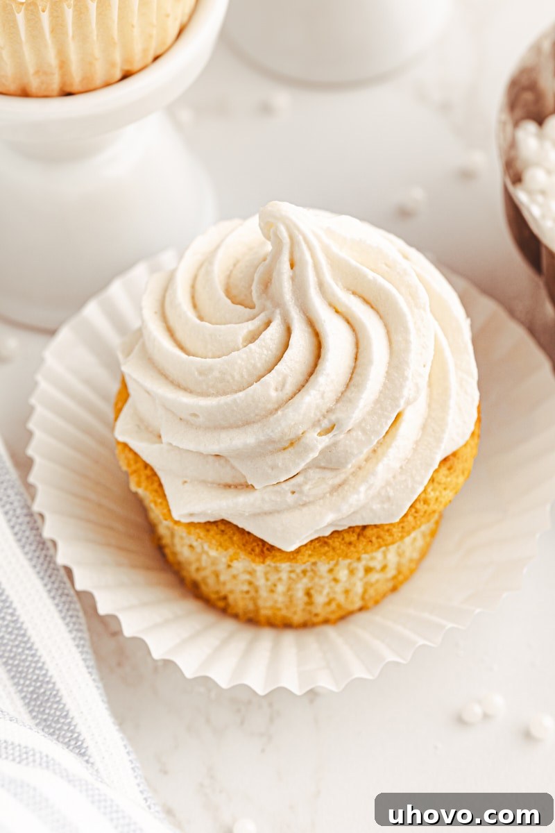 A partially unwrapped vanilla cupcake, showing its moist, fluffy interior and a hint of the frosting, inviting a bite.