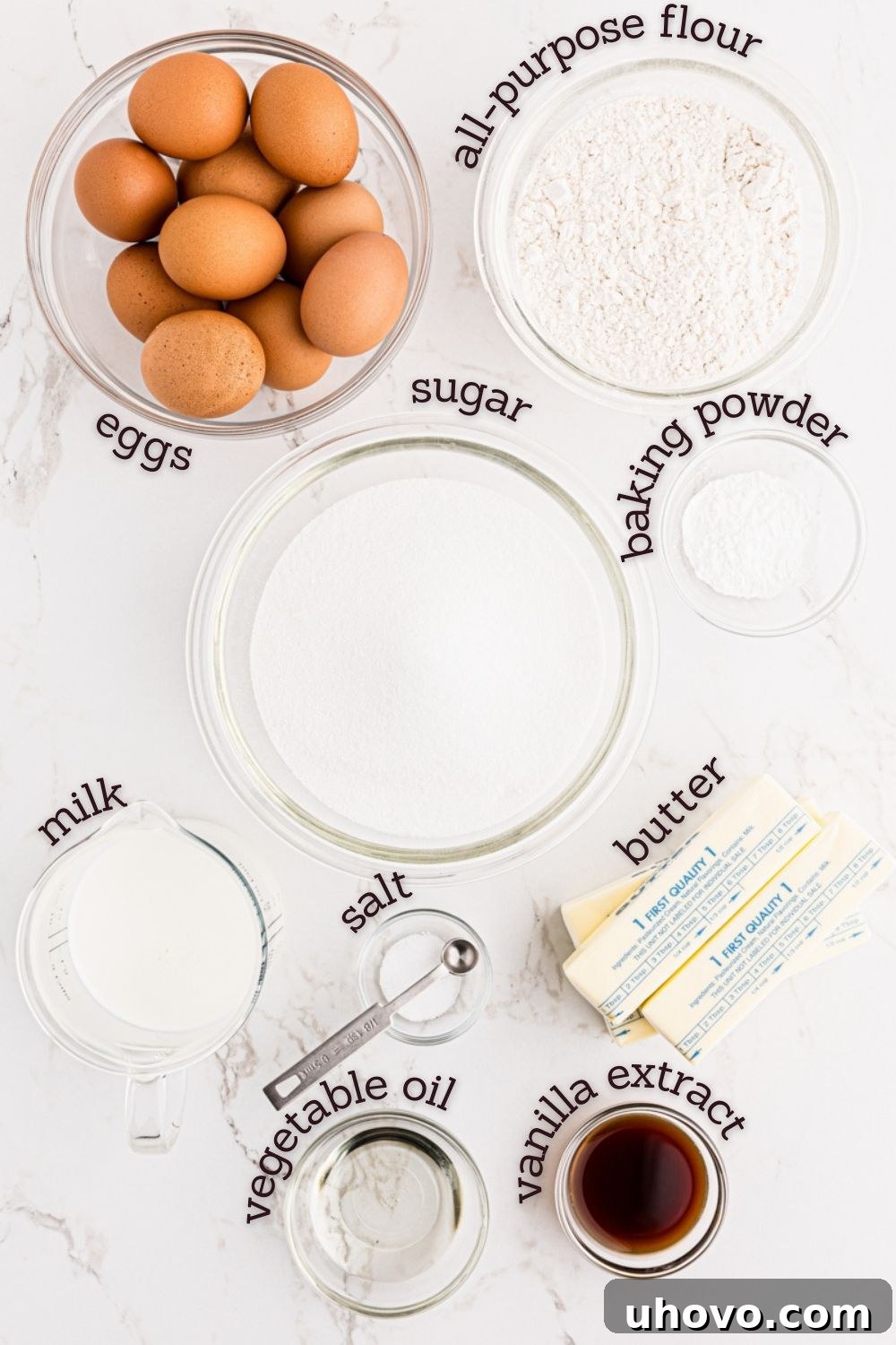 Overhead view of various fresh ingredients laid out for making vanilla cupcakes, including flour, sugar, eggs, milk, butter, and vanilla extract.