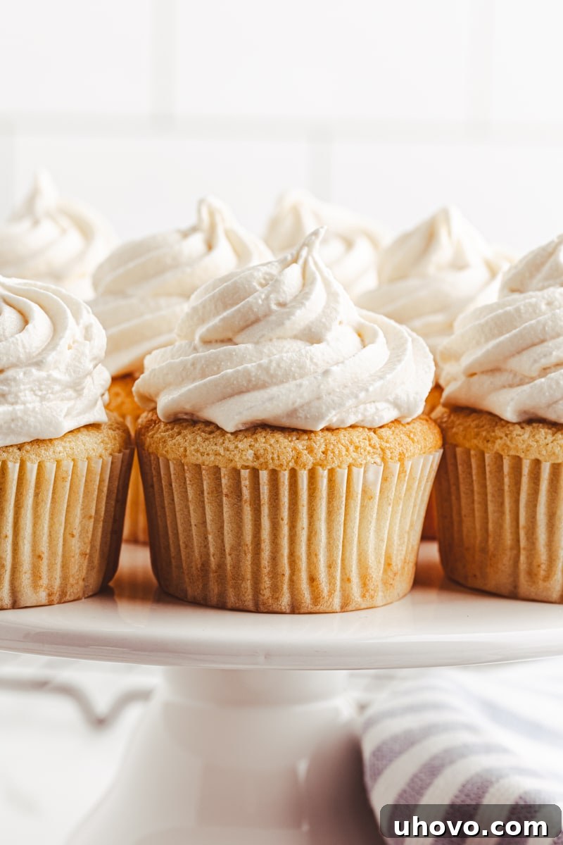A display of several beautifully frosted vanilla cupcakes on a pristine white cake stand, highlighting their delicate decoration and inviting appearance.