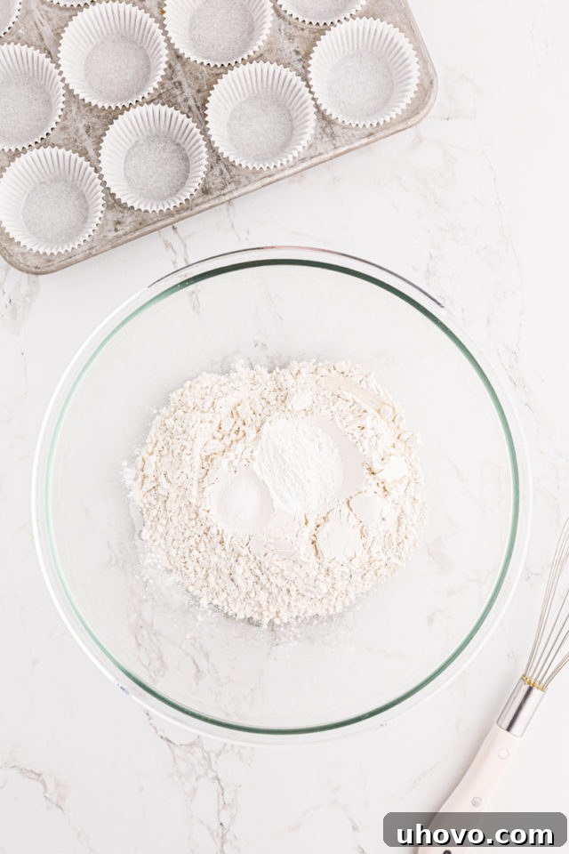 Overhead view of all-purpose flour, baking powder, and salt measured into a clear glass mixing bowl, ready to be whisked.