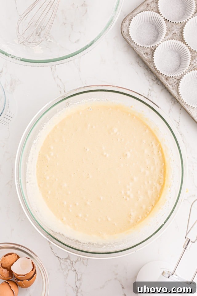 Overhead view of smooth, well-combined vanilla cupcake batter in a glass mixing bowl, indicating it's ready for baking.
