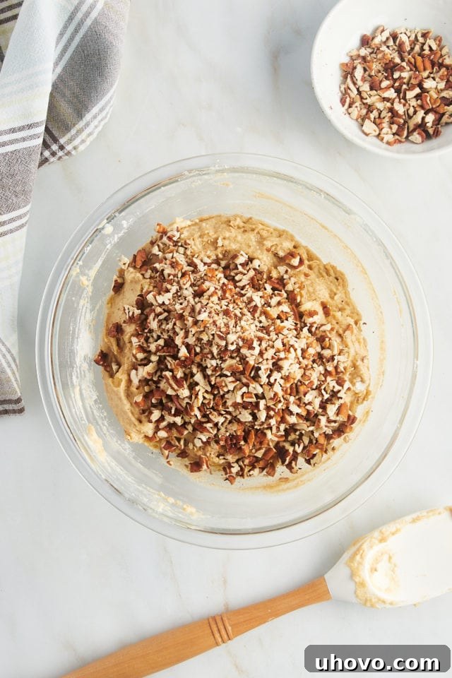Overhead view of pecans added to bowl of muffin batter