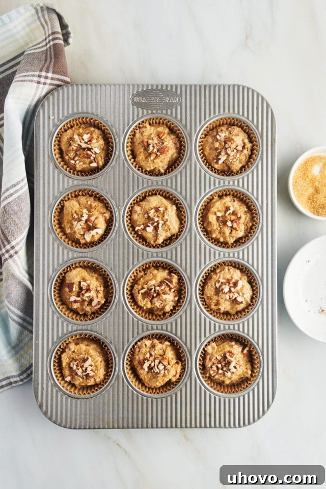 Overhead view of cinnamon pecan muffin batter in pan topped with pecans