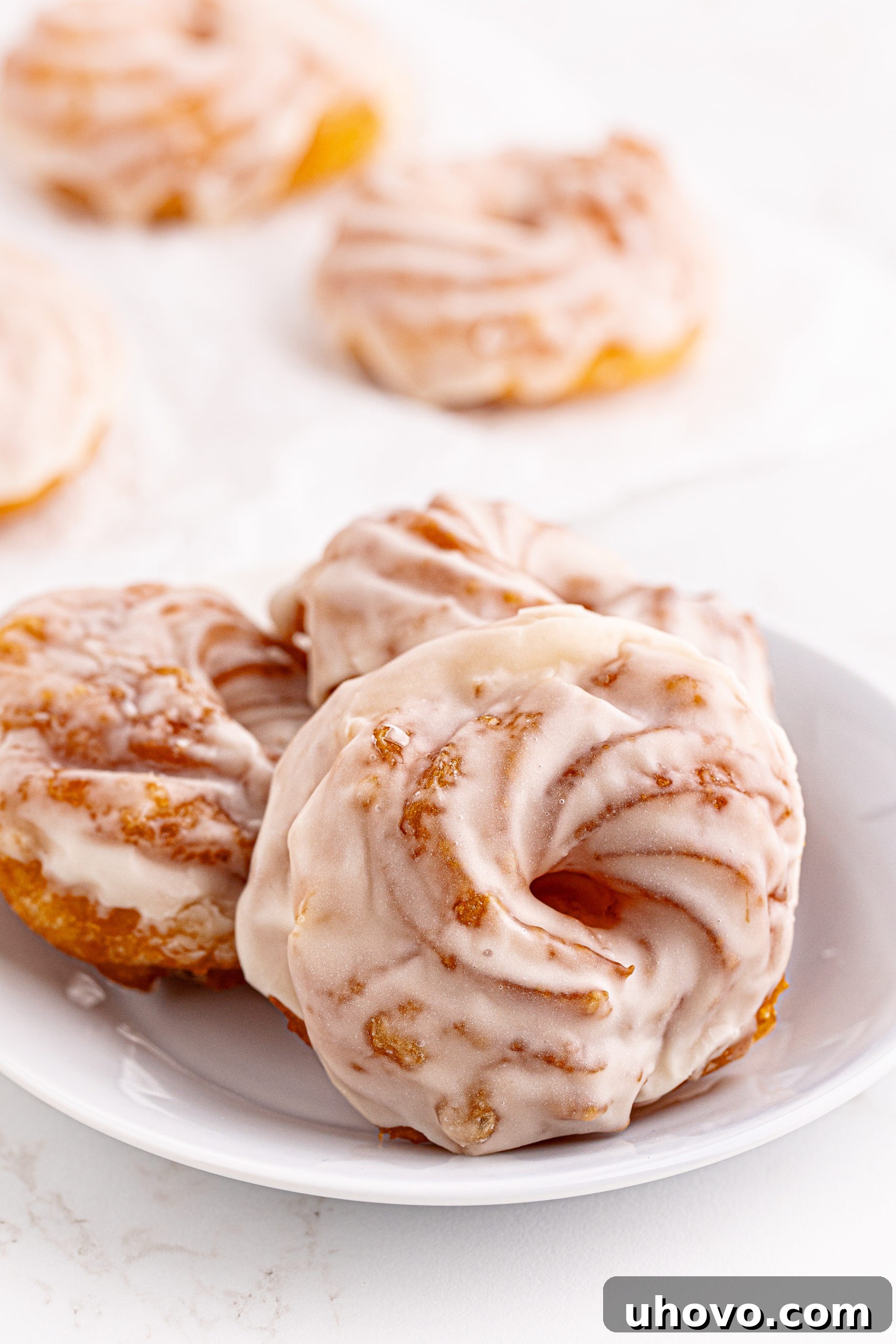 3 French crullers on white plate, with additional crullers in background