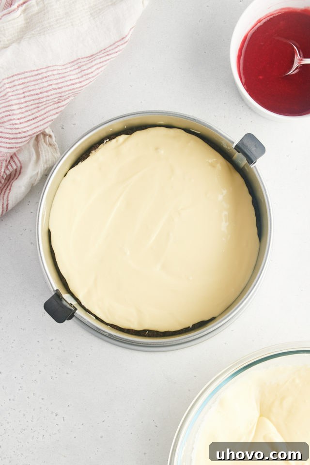 Overhead view of the first half of the smooth white chocolate cheesecake filling being carefully poured onto the cooled Oreo crust in the springform pan.