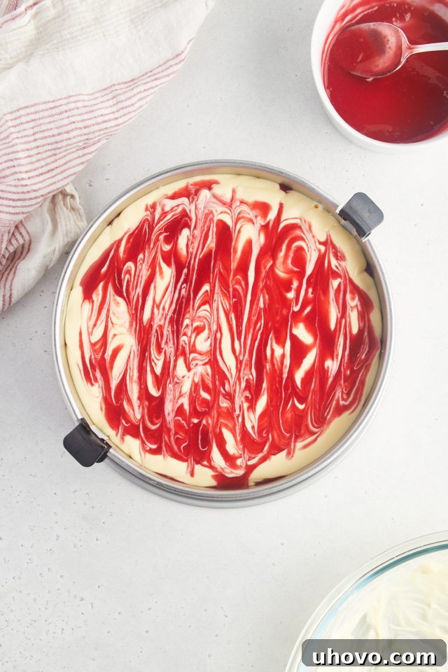 Overhead view of the unbaked white chocolate raspberry cheesecake in its pan, showcasing the intricate and beautiful raspberry sauce swirled into the top layer of the white chocolate filling.