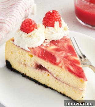 A tantalizing slice of White Chocolate Raspberry Cheesecake resting on a pristine white plate, perfectly showcasing the intricate layers of dark Oreo crust, creamy white chocolate filling, and striking red raspberry swirls. A fork is poised, ready for the first bite, emphasizing its irresistible appeal.