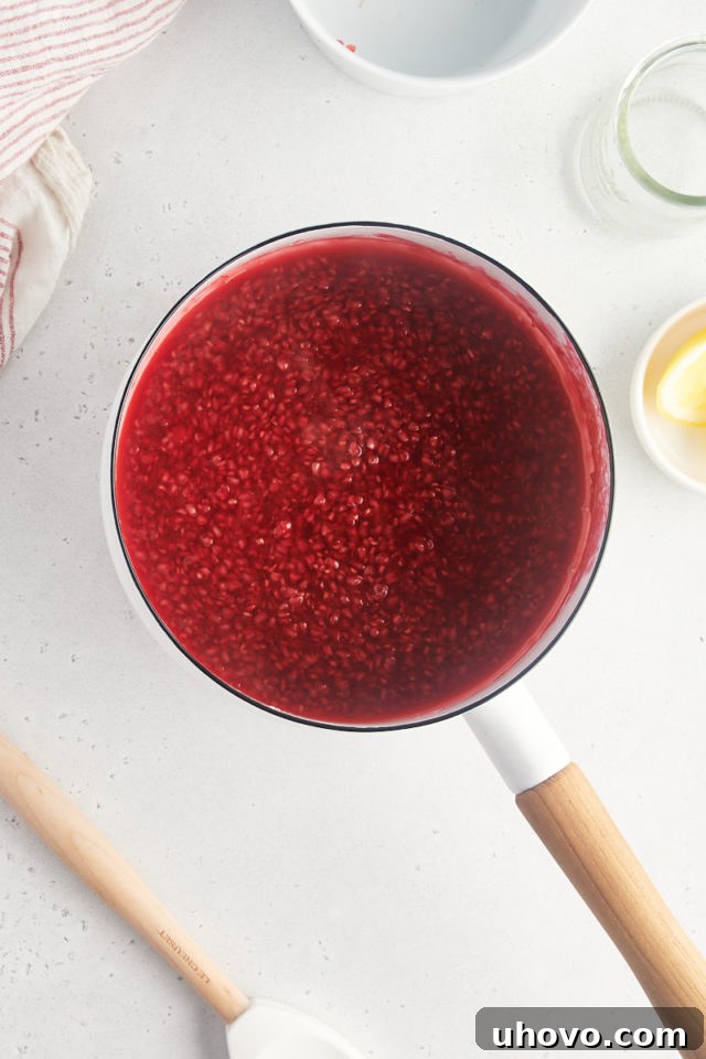Overhead view of vibrant red raspberry sauce gently simmering in a saucepan on the stovetop, thickening beautifully.