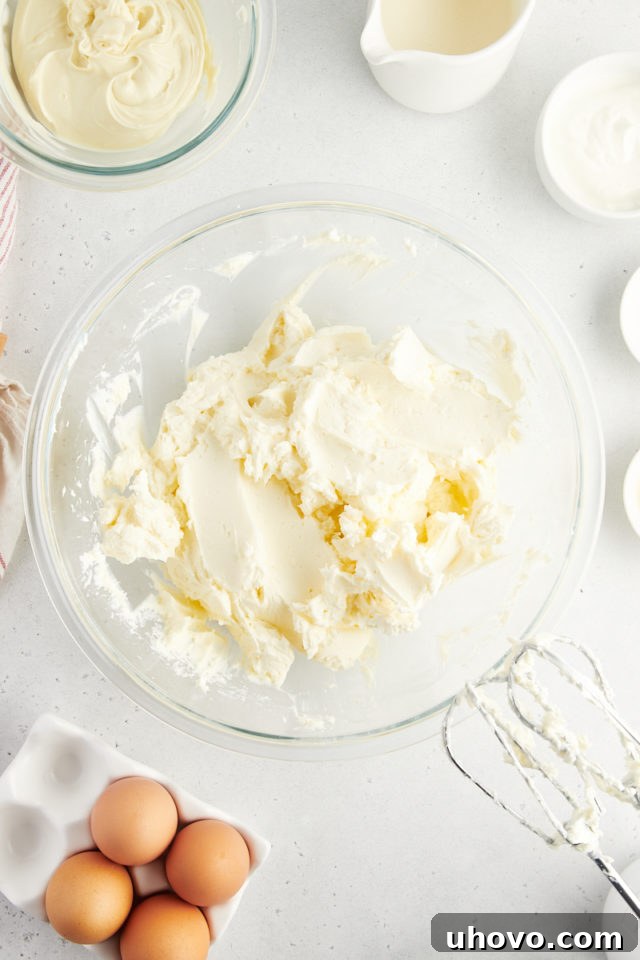 Overhead view of softened cream cheese, granulated sugar, and cornstarch being beaten in a large mixing bowl until the mixture is perfectly smooth and creamy.
