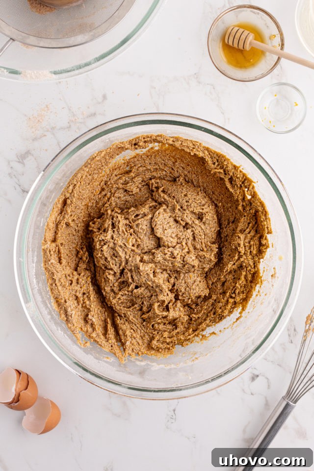 Overhead view of partially mixed morning glory muffins batter in a glass mixing bowl, before any solid mix-ins are added, showing a slightly lumpy texture.